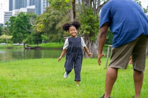Happy mixed race family in park. African father playing and hugging together with little daughter at public park. Dad and child girl kid enjoy and having fun outdoor lifestyle activity in summer.