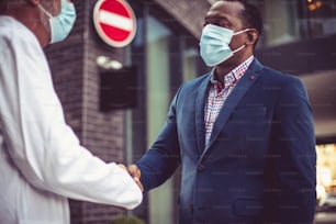 Business man, and doctor on street handshaking. Wearing protective mask. Focus background.