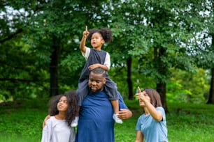 Happy mixed race family in park. African father and Asian mother with two little daughter holding hands walking together in garden. Mom and dad with child girl kid enjoy and having fun in outdoor lifestyle activity.