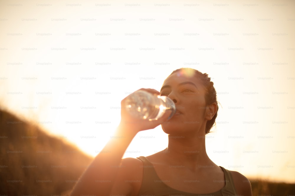 Sportliche junge Frau trinkt Wasser im Freien.