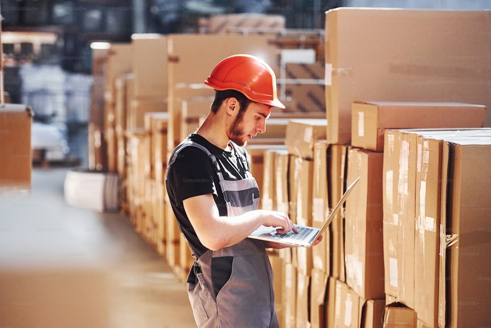 Un travailleur de stockage en uniforme et un ordinateur portable moderne dans les mains vérifie la production.