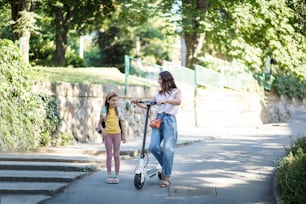 This is so fun thing.  Mother and daughter together in the park. Woman riding scooter.