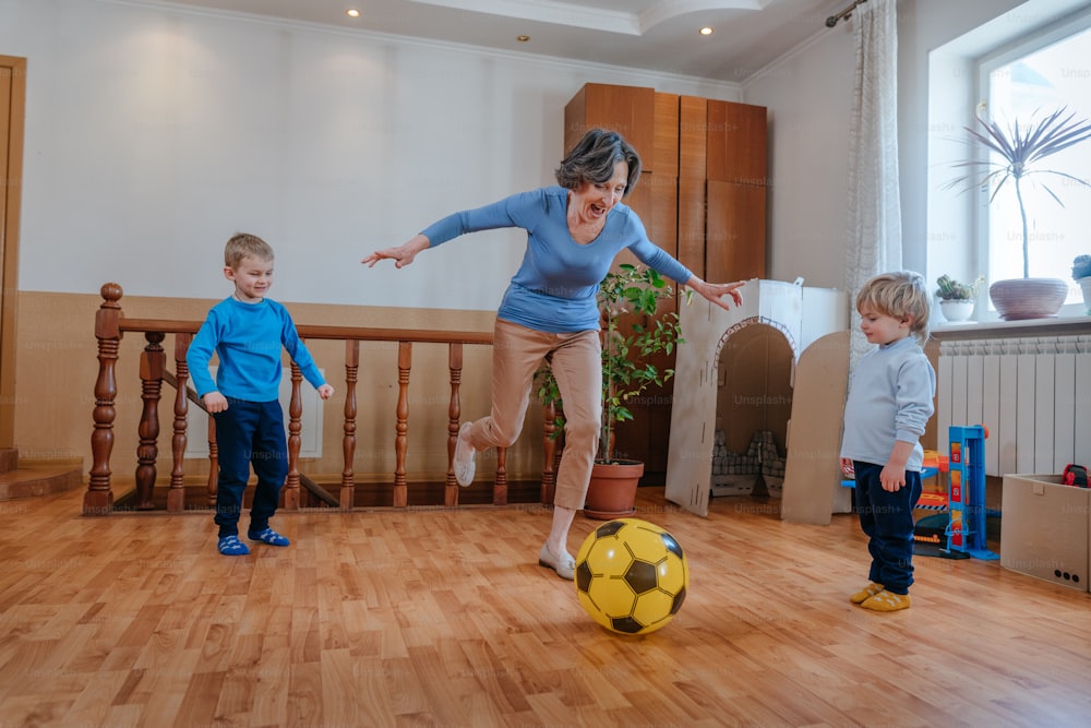 Abuela activa jugando a la pelota con sus nietos en la habitación de los niños en el interior. Enfoque selectivo.