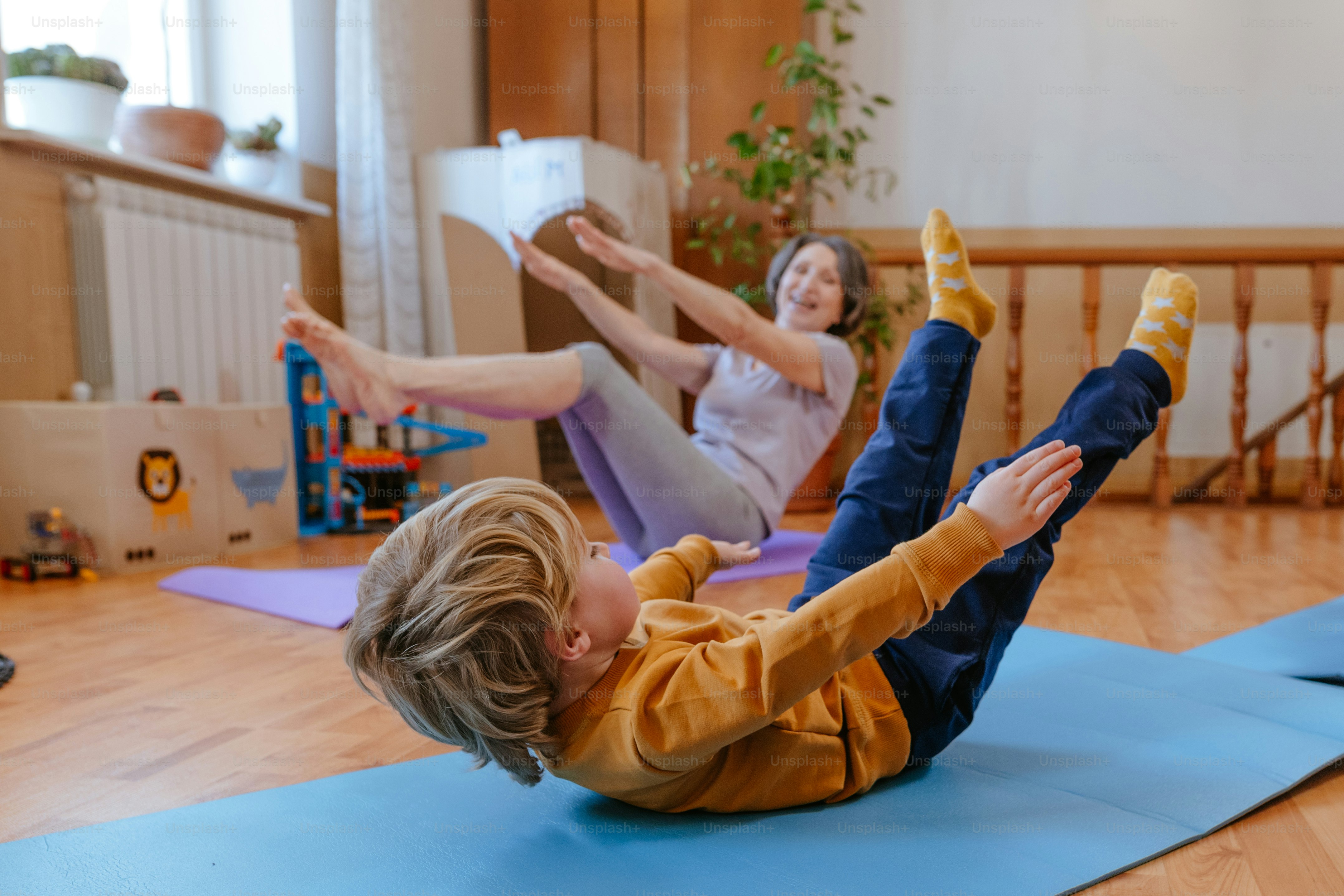Little 3 years old boy doing exercises with his grandmother in the kids room. Selective focus.