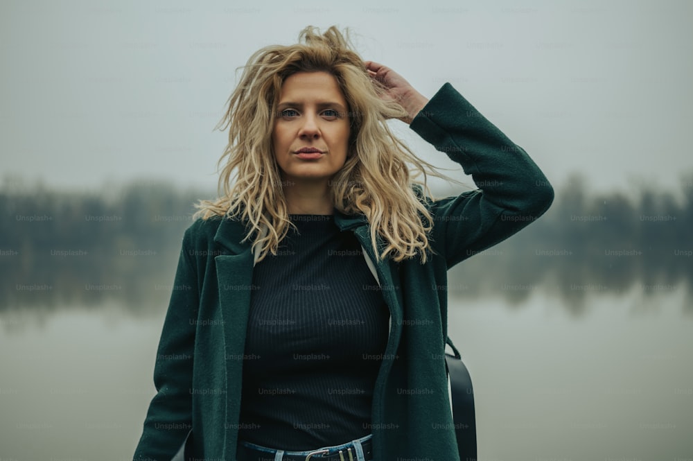 Portrait of a beautiful blonde woman posing in the nature wearing a green coat