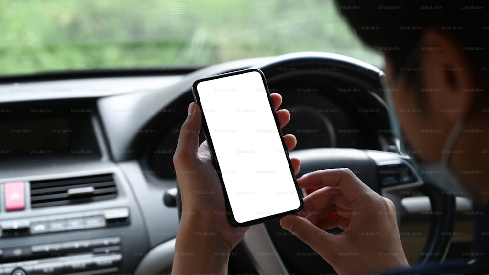 Close up view of young asian man wearing protective mask and using mobile phone while sitting in his car.