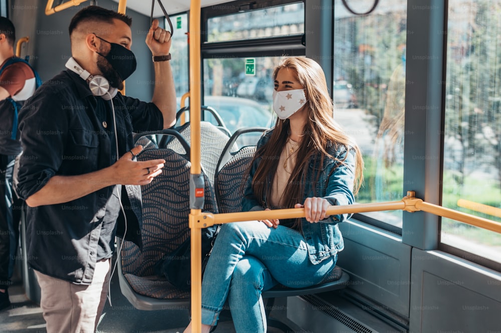 Ein Paar Freunde treffen sich in einem Bus, während sie aufgrund einer Pandemie eine Gesichtsschutzmaske tragen