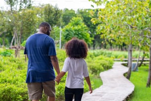 Happy mixed race family in park. African father with little daughter holding hand and walking together in the garden. Dad and child girl kid enjoy and having fun in summer outdoor activity vacation