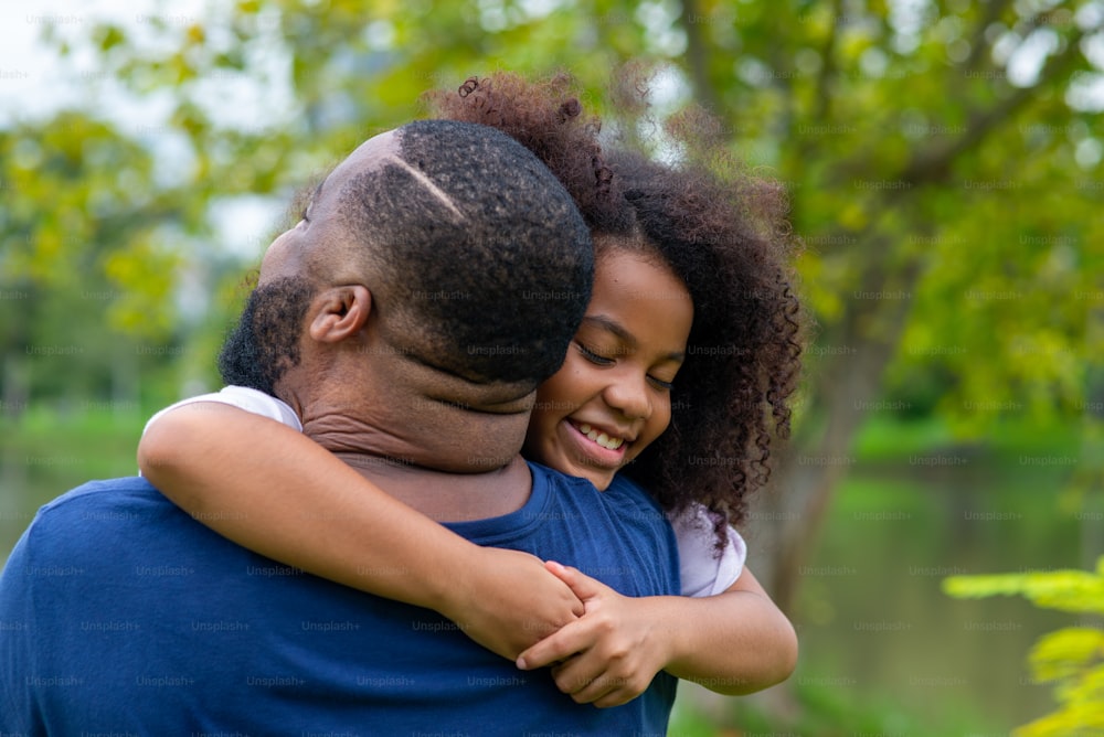 Happy mixed race family in park. African father playing and hugging together with little daughter at public park. Dad and child girl kid enjoy and having fun outdoor lifestyle activity in summer.