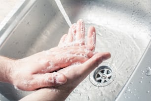 Mains savonnantes masculines à côté de verser de l’eau à un évier de cuisine