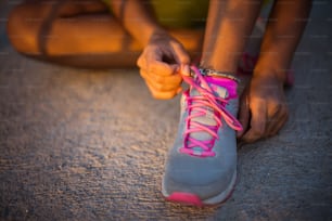 Deportista africana irreconocible atando los cordones de los zapatos en las zapatillas. Cerrar.