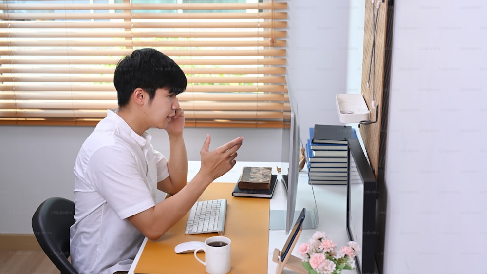 Young asian man talking on mobile phone with his business partner while sitting at comfortable office.