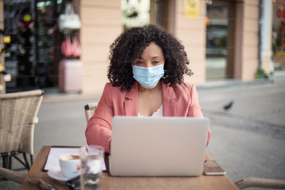 Business woman with protective face mask working in café.