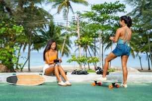 Asian woman with girl friends wearing safety skateboarding gloves for skating at skateboard park. Happy female friendship enjoy summer outdoor active lifestyle play extreme sport surf skate together