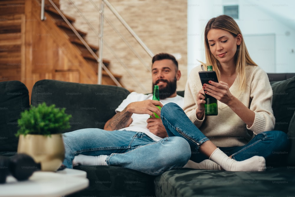 Young attractive couple chilling at home while drinking beer and watching television