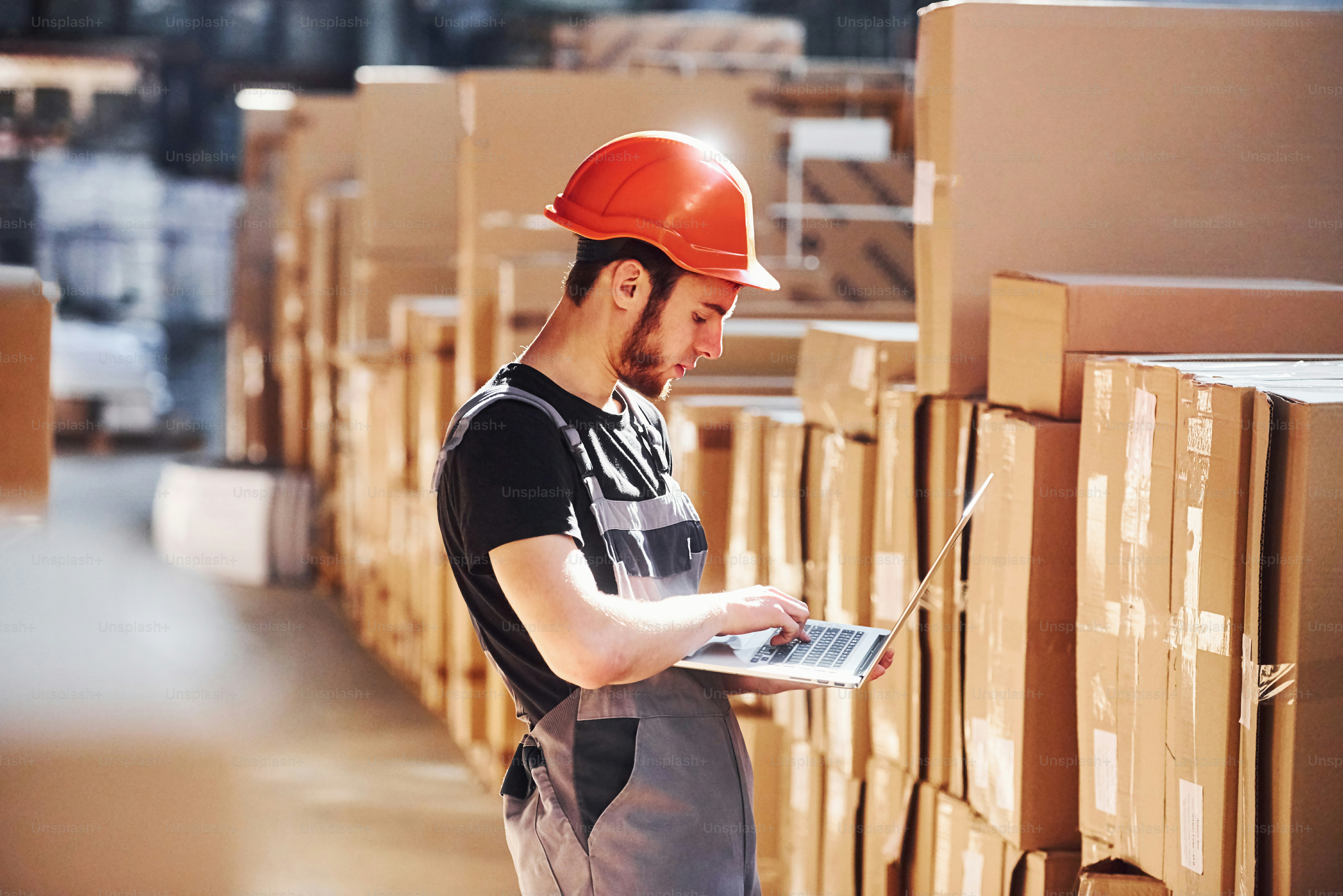 Addetto al deposito in uniforme e laptop moderno in mano controlla la produzione.