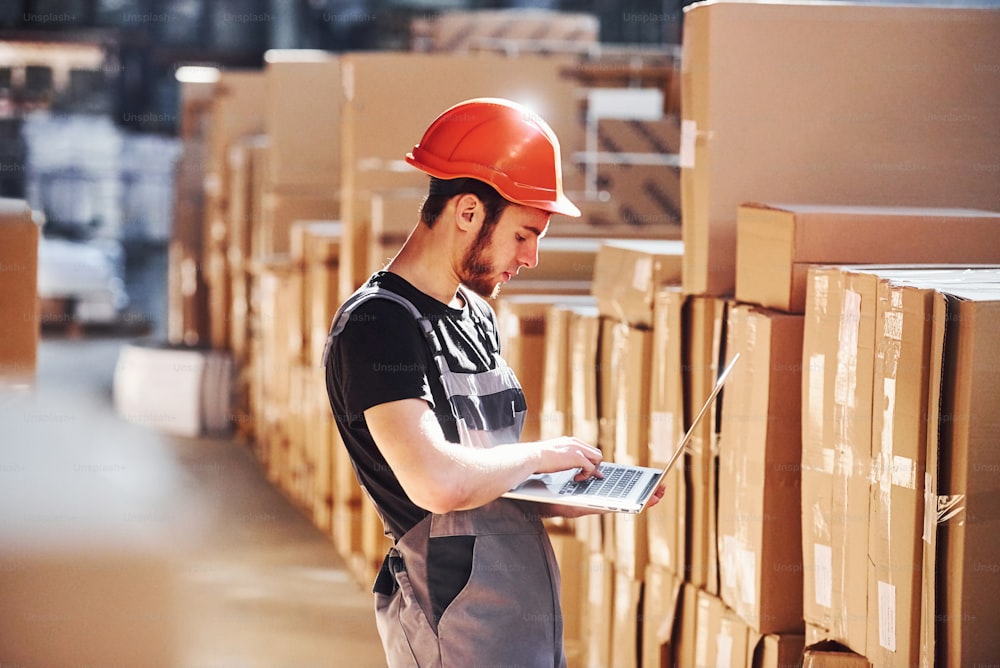 Storage worker in uniform and modern laptop in hands checks production.