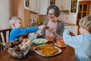 Grandchildren treating their grandmother with cookies at the kitchen. Selective focus.