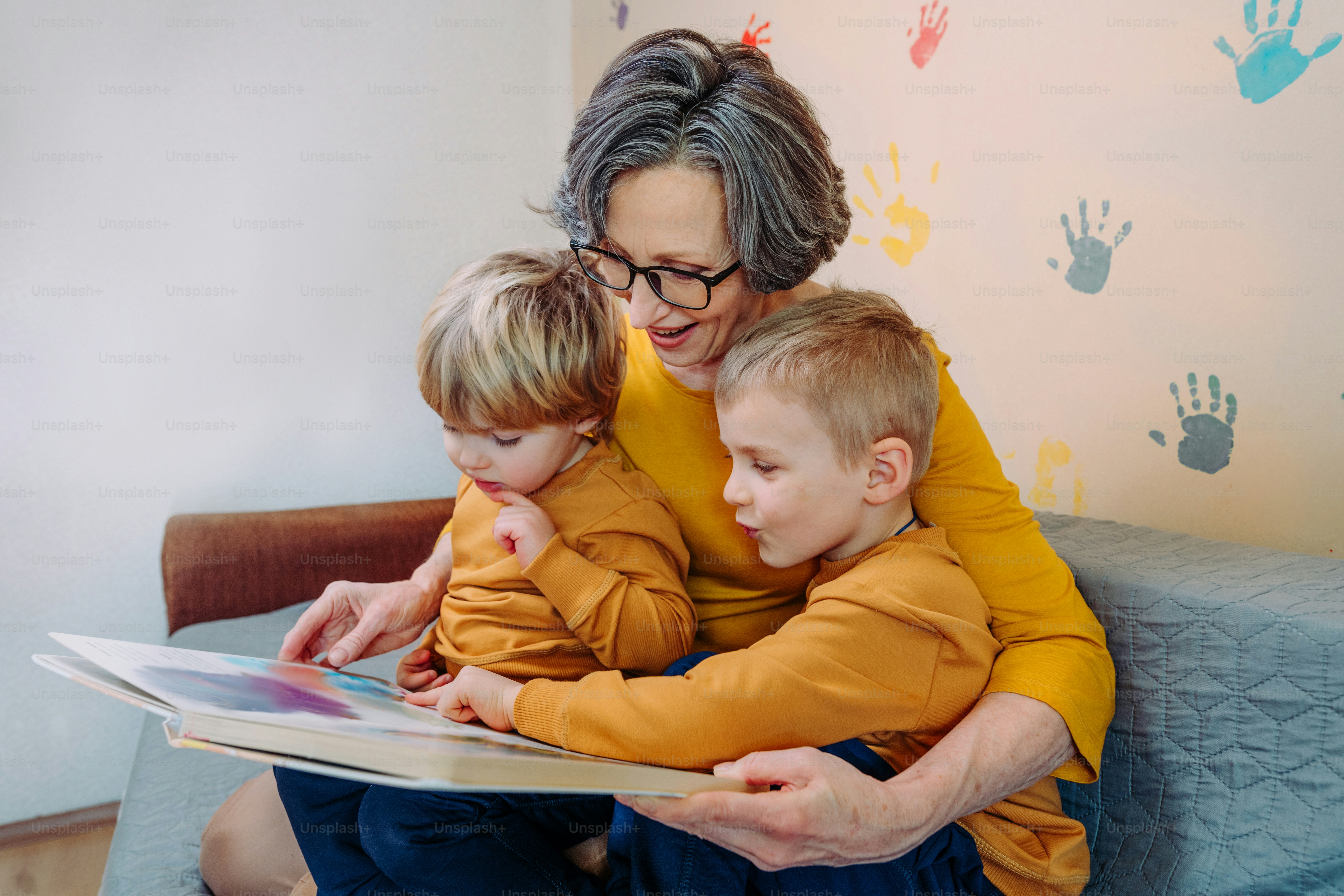 Grandmother having fun time with her grandchildren reading book in the kids room indoor. Selective focus.
