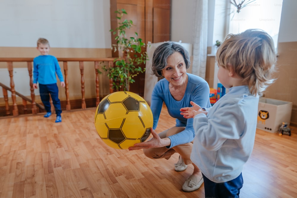 Abuela activa jugando a la pelota con sus nietos en la habitación de los niños en el interior. Enfoque selectivo.
