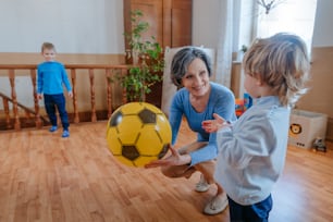 Active grandmother playing the ball with her grandchildren in the kids room indoor. Selective focus.