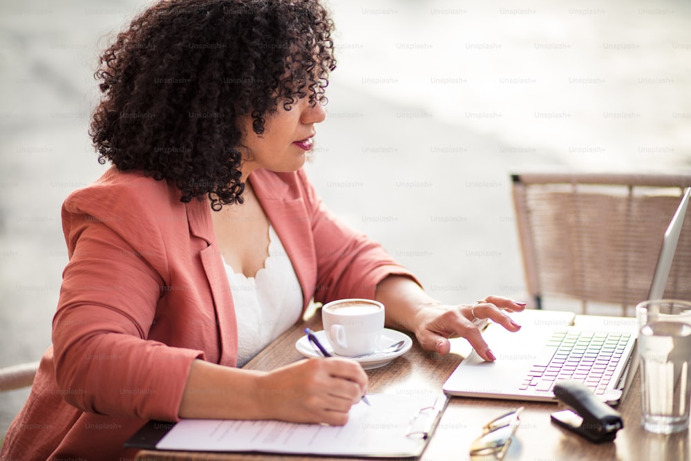 Empresária mestiça usando um laptop sentado em um café. Mulher de negócios sentada no café e usando laptop.