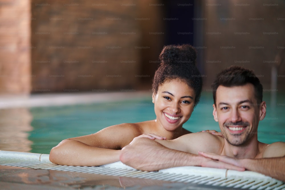 Retrato do jovem casal feliz na piscina interior, olhando para a câmera.