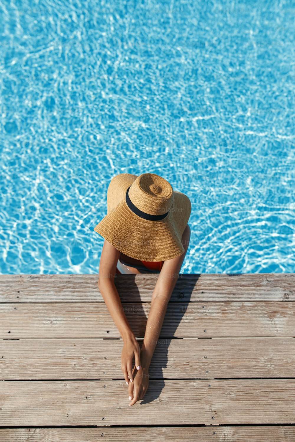 Mulher bronzeada bonita no chapéu relaxando na água da piscina no cais de madeira, desfrutando de férias de verão, vista superior. Fêmea jovem e esbelta tomando sol na elegante borda da piscina. Espaço para texto. Viagens e Férias