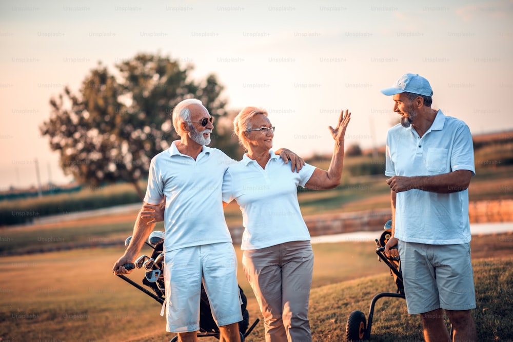 Drei ältere Golfer spazieren und unterhalten sich.