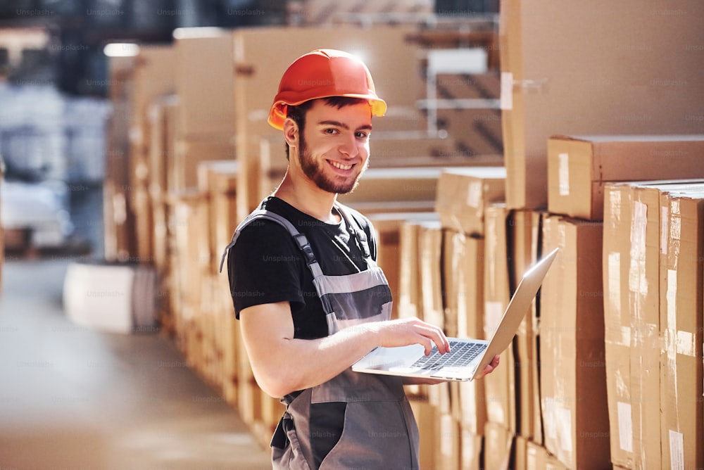 Storage worker in uniform and modern laptop in hands checks production.