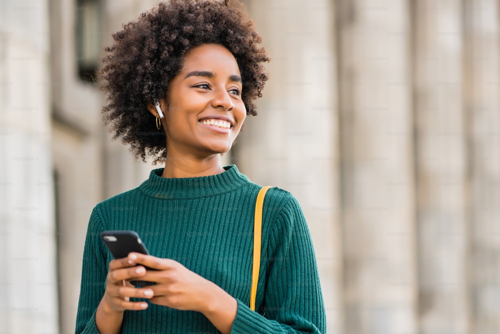 Portrait of afro business woman using her mobile phone while standing outdoors at the street. Business and urban concept.