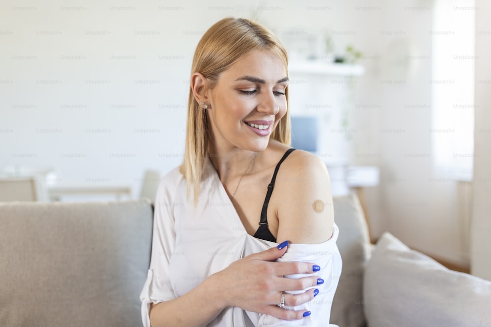 Ritratto di una donna sorridente dopo aver ricevuto un vaccino. Donna che tiene abbassata la manica della camicia e mostra il braccio con la benda dopo aver ricevuto la vaccinazione.