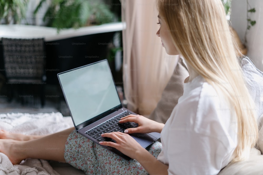Blogueuse pour jeunes adultes assise sur un lit confortable en pyjama, créez du contenu pour son blog en ligne sur un ordinateur portable. Femme regardant le moniteur de l’espace de copie et passant la matinée à la maison dans une chambre confortable et lumineuse