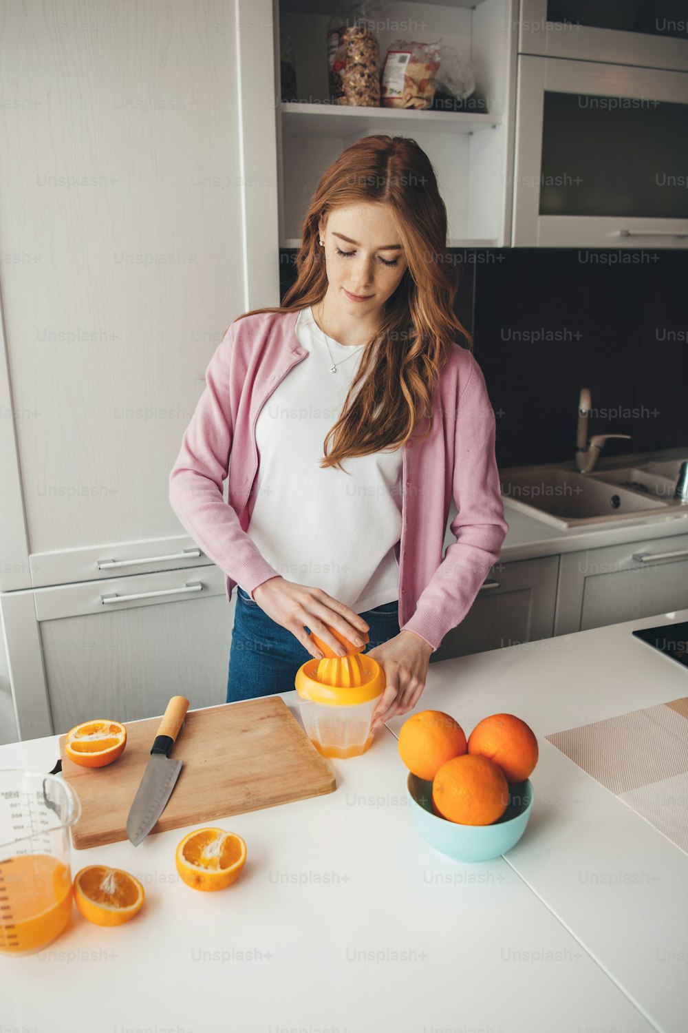 La donna zenzero con le lentiggini sta spremendo il succo d'arancia naturale a casa in cucina