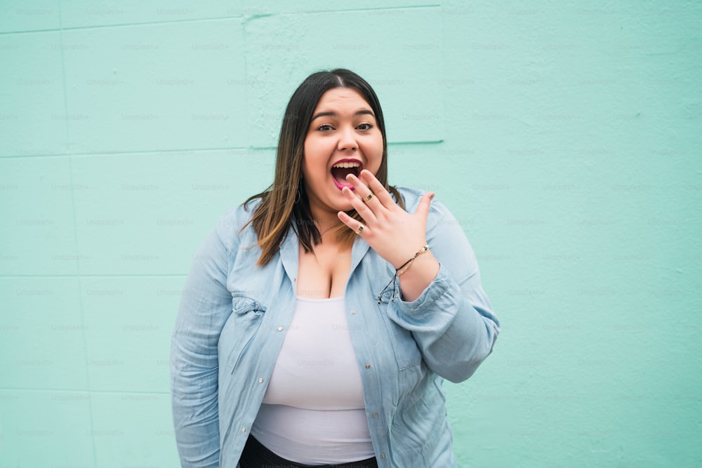 Portrait of young pluse size woman with a shocked expression while standing against light blue wall outdoors.