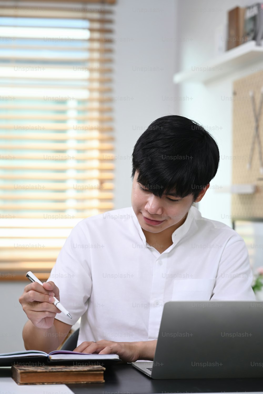 Portrait of young man freelancer sitting infant of laptop and writing information on digital tablet.