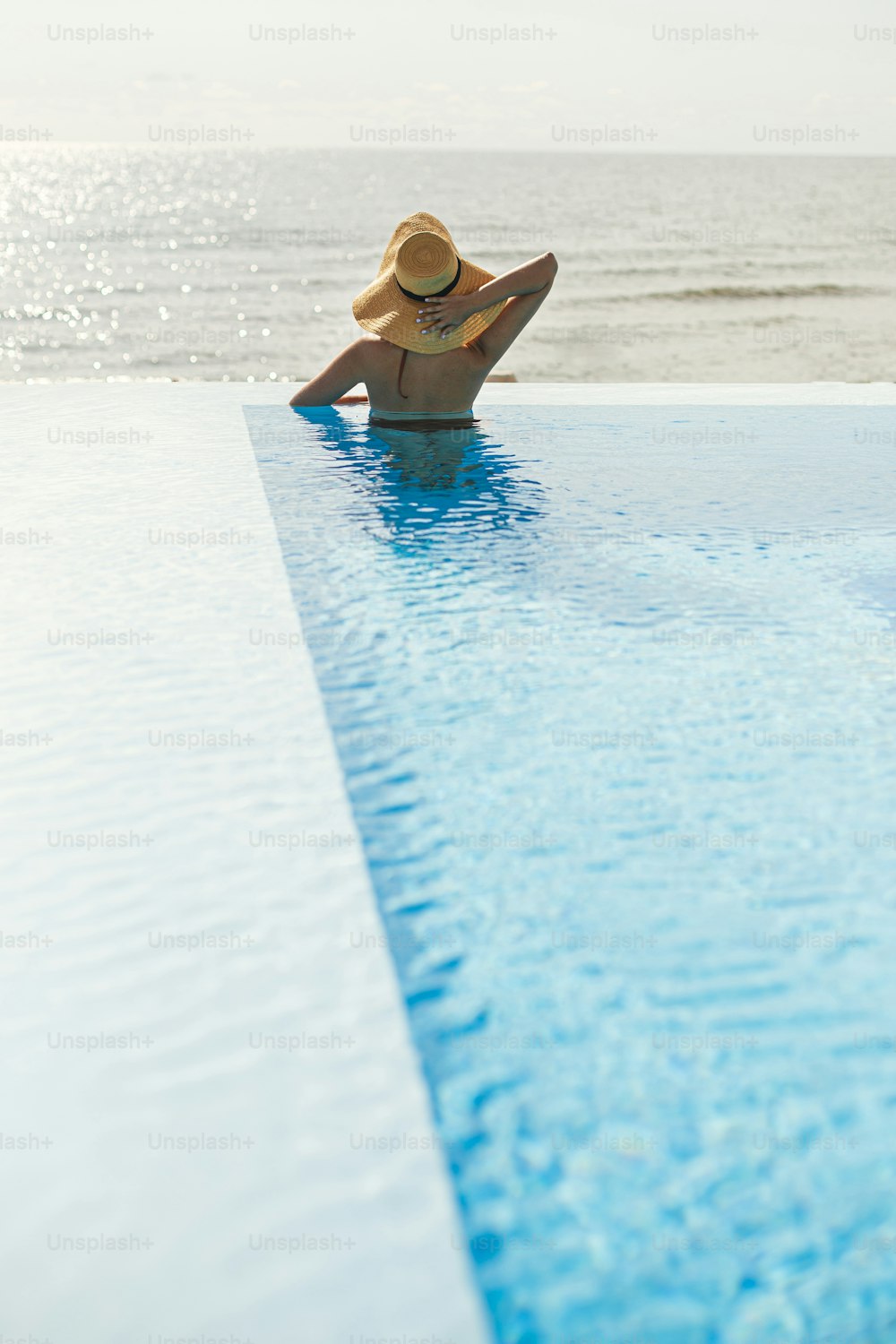 Beautiful woman in hat relaxing at edge in blue pool, enjoying summer vacation and sea view. Slim young female relaxing at tropical resort in swimming pool. Travel and Holidays. Space for text