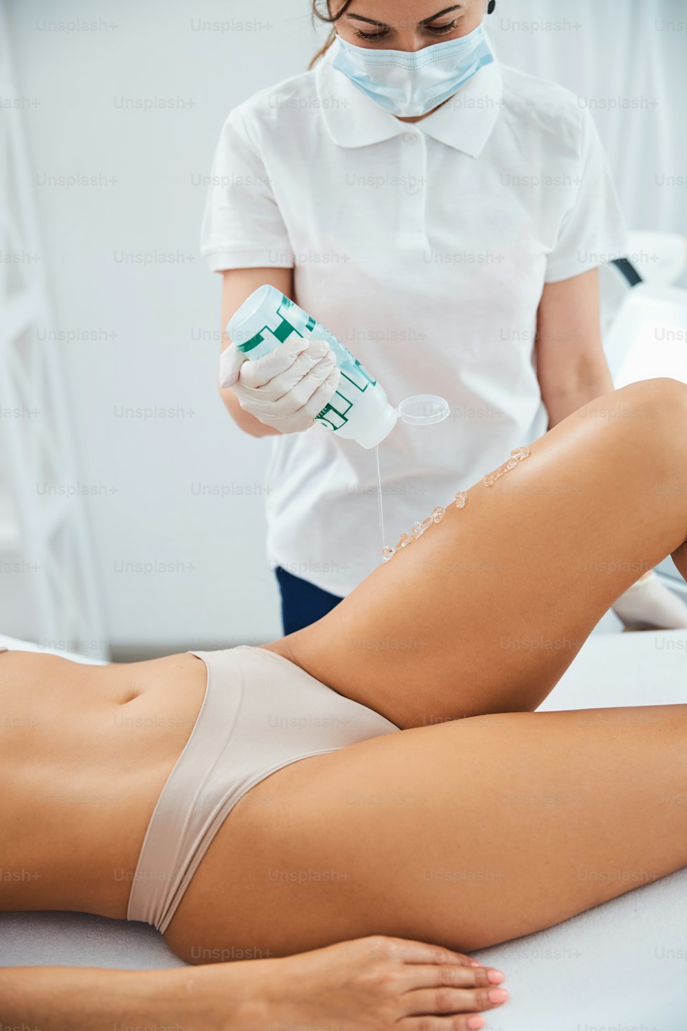 Medico focalizzato che versa il gel ad ultrasuoni trasparente da una bottiglia sulla pelle della donna caucasica