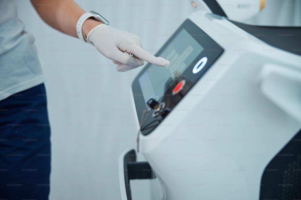 Cropped photo of a professional dermatologist in a nitrile glove setting the treatment parameters before a cosmetic procedure