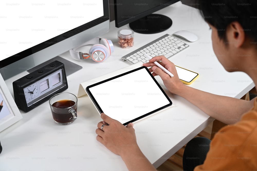 Over shoulder view of man sitting at home office desk and surfing internet on digital tablet.