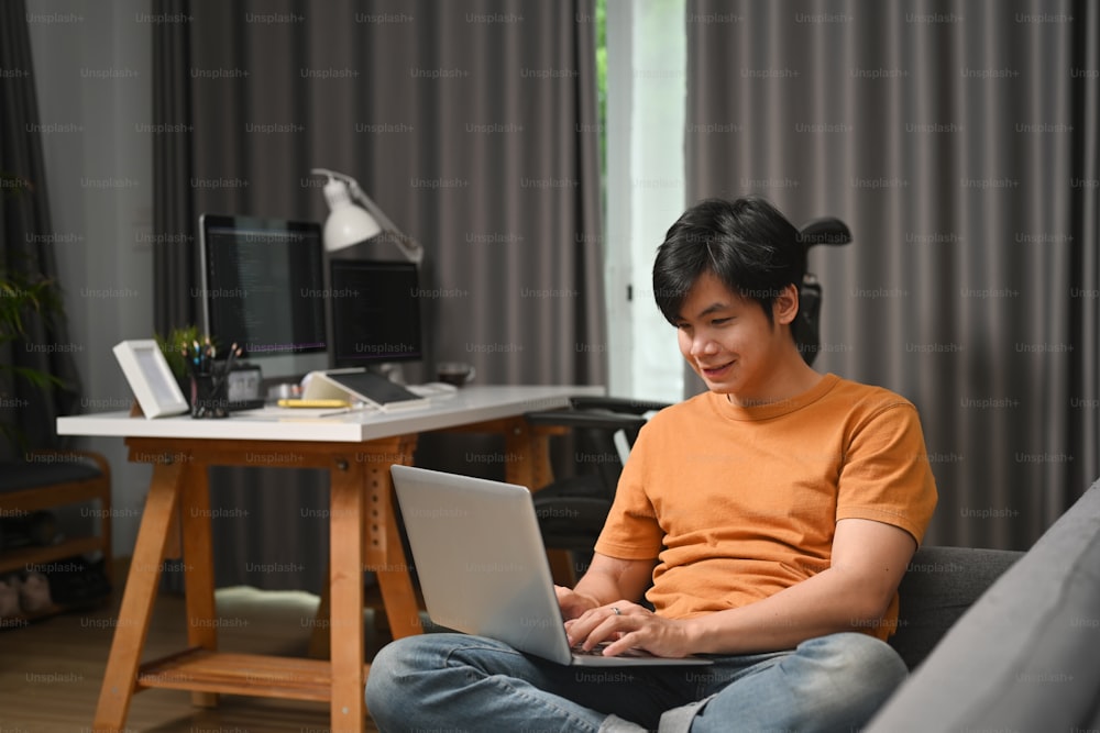 Happy casual man freelancer using laptop while sitting on sofa.