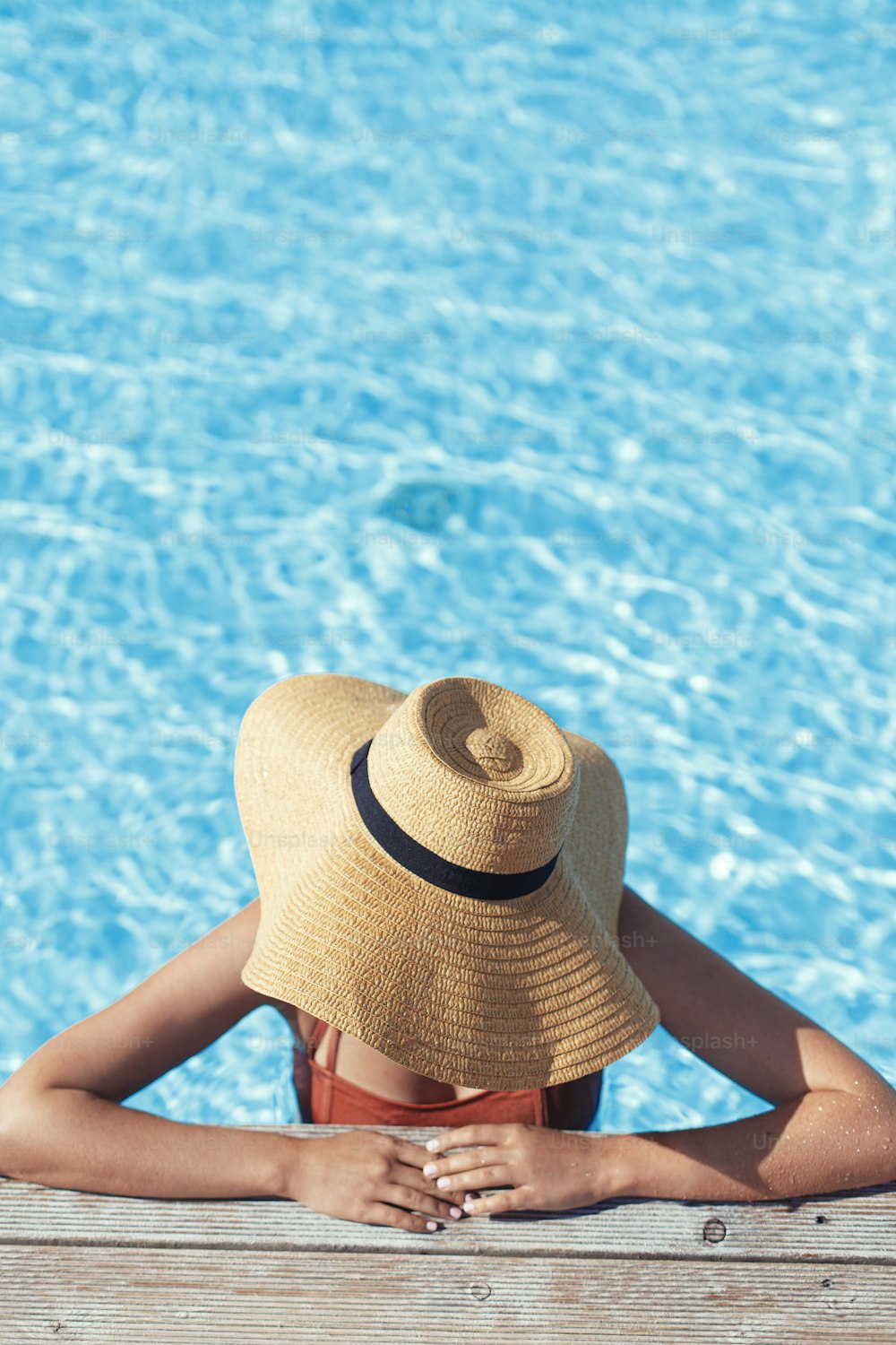 Bella donna in cappello che si rilassa al molo di legno della piscina in acqua, godendo delle vacanze estive in un resort tropicale. Giovane femmina magra che prende il sole sul bordo della piscina, vista sopra. Vacanze e viaggi