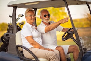 Elderly golf couple rides in a golf cart.
