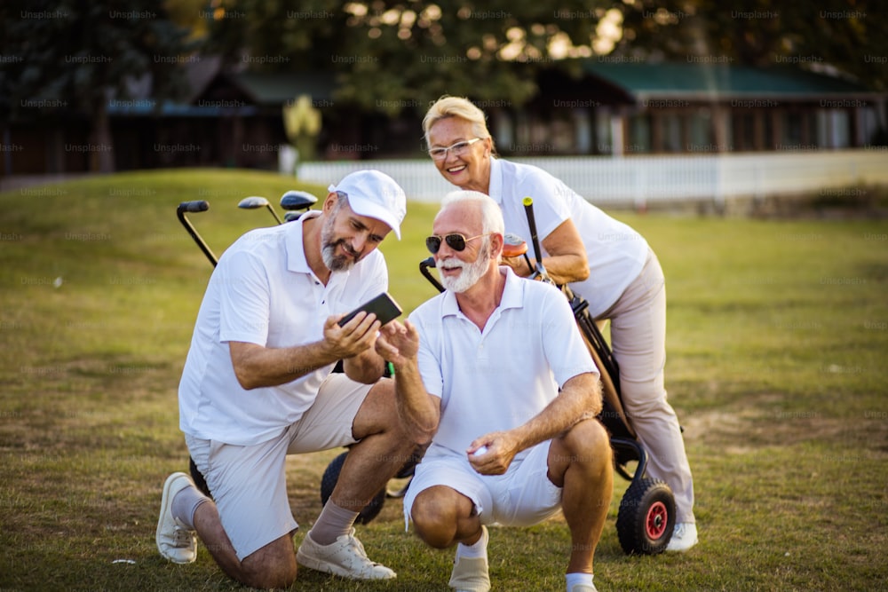 Golfistas seniores em quadra. Dois homens usando telefone inteligente.