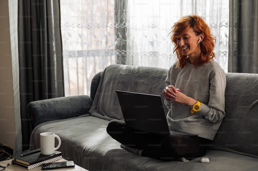 Young redhead woman using a laptop while working from home and sitting on a couch
