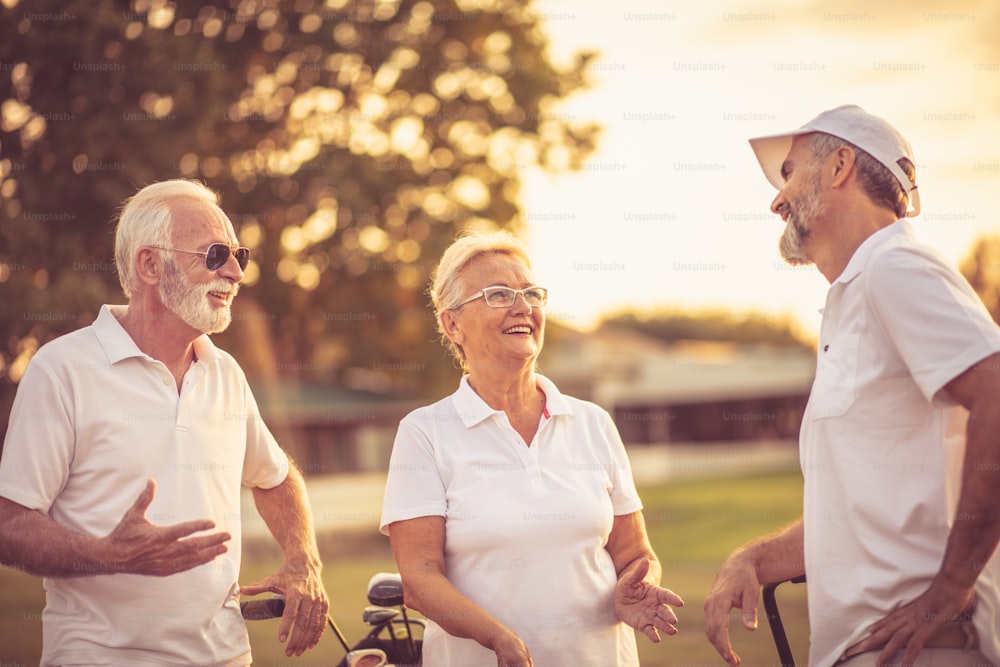Tre golfisti anziani sorridenti che parlano sul campo da golf.