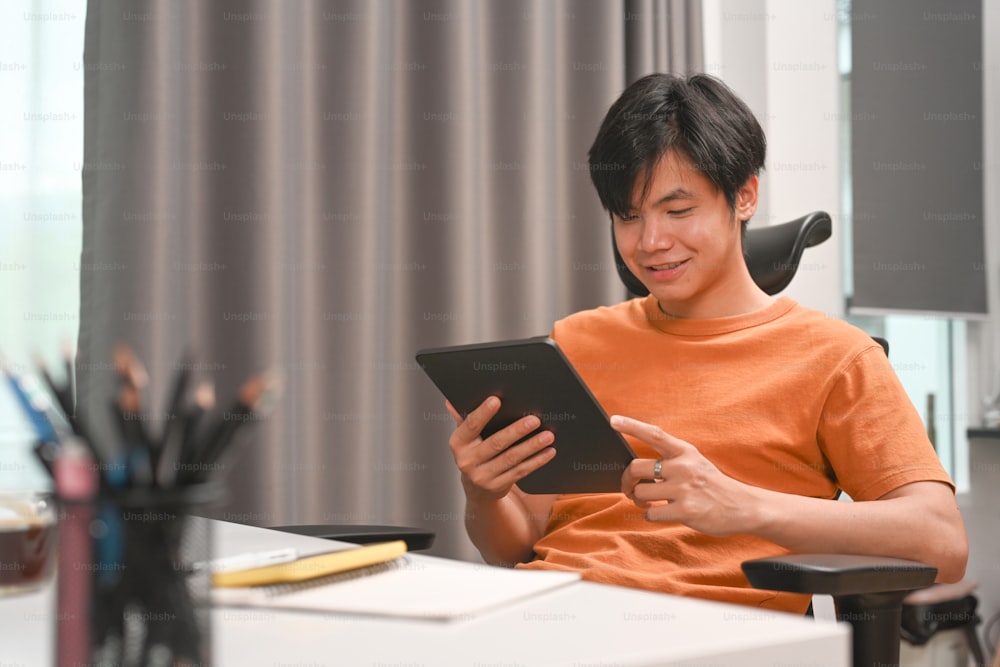 Happy young man freelancer sitting on chair in home office and using digital tablet.
