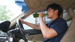 Uomo che beve birra mentre guida un'auto. Guida in stato di ebbrezza.