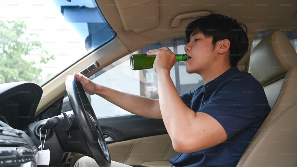 Uomo che beve birra mentre guida un'auto. Guida in stato di ebbrezza.