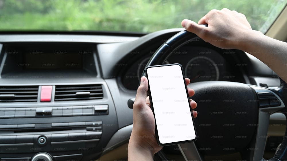 Vista de cerca de un joven que usa un teléfono inteligente mientras conduce un automóvil.